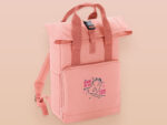 Pink roll top twin handle backpack with an embroided design of cute space alien cat floating in the stars and the quote beam me up I want to leave!