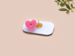 A clear acrylic pin badge with a pink heart-shaped pin back clasp. The design of the pin badge is of a cute chibi penguin dancing in a suit under a spotlight with the quote give 'em the ol' razzle dazzle