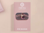 A clear acrylic pin badge with a pink heart-shaped pin back clasp. The design of the pin badge is of a cute chibi penguin dancing in a suit under a spotlight with the quote give 'em the ol' razzle dazzle