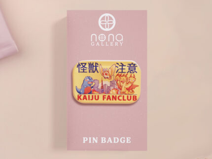 A clear acrylic pin badge with a pink heart-shaped pin back clasp. The design of the pin badge is of a cute chibi blue godzilla like kaiju mothra and King Ghidorah destroying a city with the quote kaiju fanclub and kaiju warning in japanese kanji