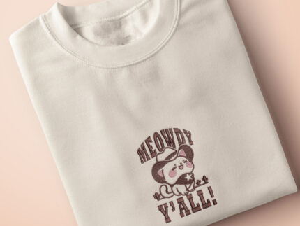 A cream crew neck short sleeve t-shirt, with an embroidered brown thread design of a cute cowboy cat with hat surrounded by the quote meowfy ya'll!