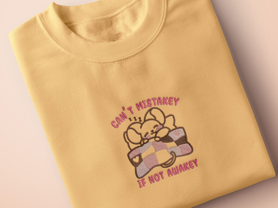 Yellow t-shirt with an embroidered mouse sleeping under a patchwork blanket with the text can't mistakey if not awakey
